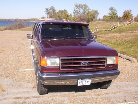 1988 Ford C-350 (Centurion Conversions) - A burgundy Ford F-Series truck is parked in a lot near a body of water on a sunny day.