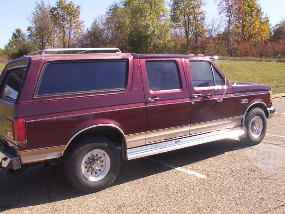 Maroon extended cab pickup truck with a camper shell, tan lower trim, and chrome running boards