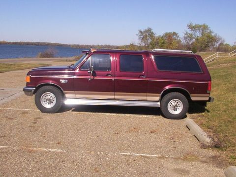 1988 Ford C-350 (Centurion Conversions) - Maroon Ford Bronco Centurion Conversion SUV parked next to a body of water on a sunny day.