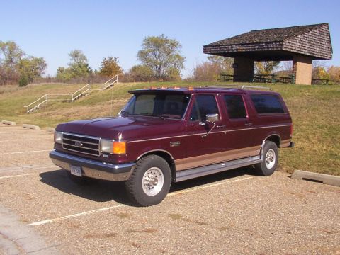 1988 Ford C-350 (Centurion Conversions) - A maroon Ford SUV conversion with tan trim is parked in a lot near a covered picnic area.