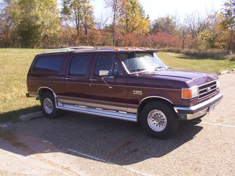 1988 Ford C-350 (Centurion Conversions) - A maroon Ford F-series SUV conversion is parked in a lot with trees in the background.