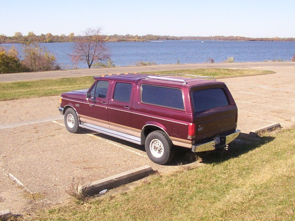 Maroon extended cab pickup with camper shell parked by a lake
