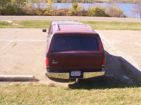 1988 Ford C-350 (Centurion Conversions) - Maroon Ford Econoline van with camper shell parked in a lot near a body of water.