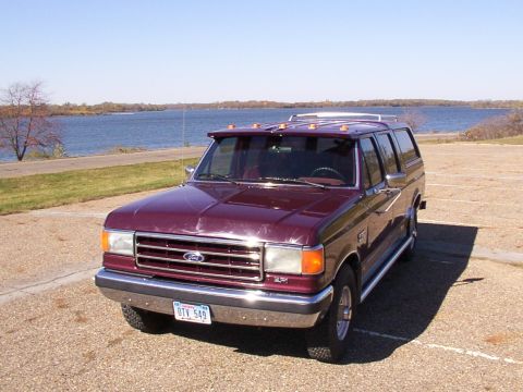 1988 Ford C-350 (Centurion Conversions) - This maroon SUV, possibly a conversion, is parked in a lot next to a body of water under a clear blue sky.