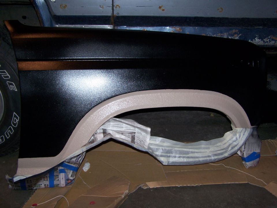 Black truck fender with primered wheel arch lying in a workshop