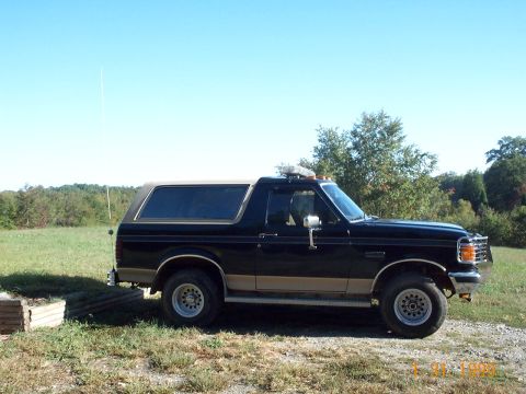 1990 Ford Bronco - A black Ford Bronco is parked outdoors on a sunny day, with trees and a field visible.