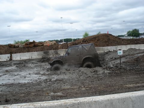 1988 Suzuki Samurai - A Suzuki Samurai navigates a muddy obstacle course under a cloudy sky.