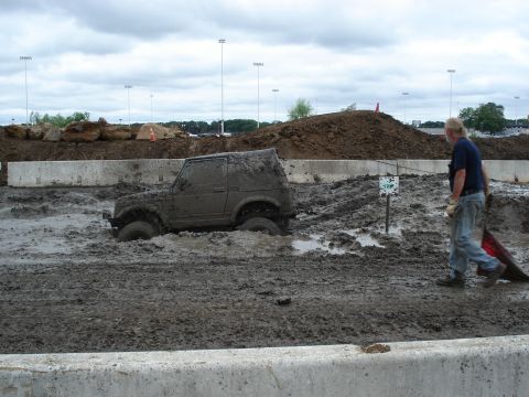 1988 Suzuki Samurai - A Suzuki Samurai is stuck in a mud bog, with a person walking past the scene.