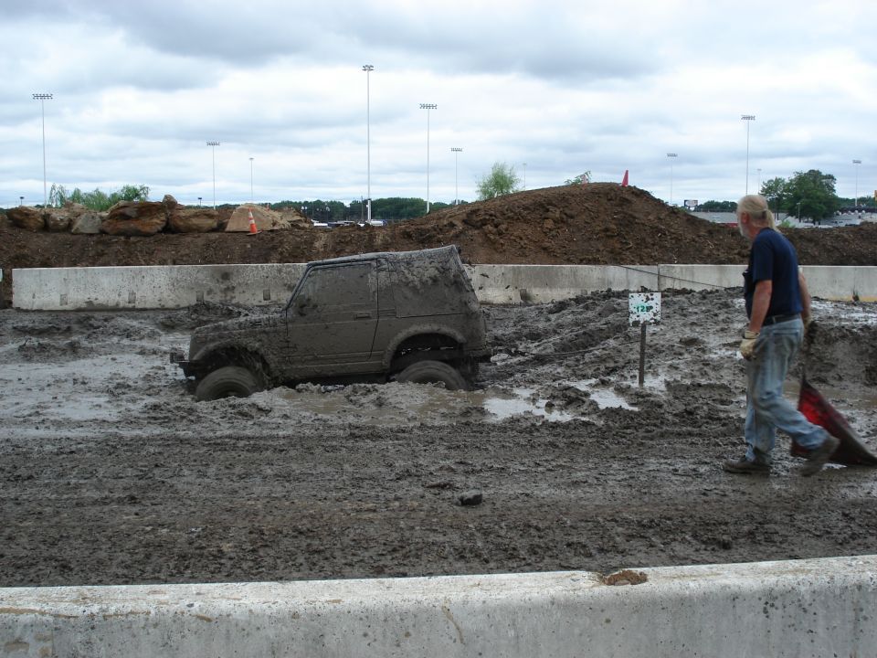 1988 Suzuki Samurai stuck deep in mud with a person walking nearby