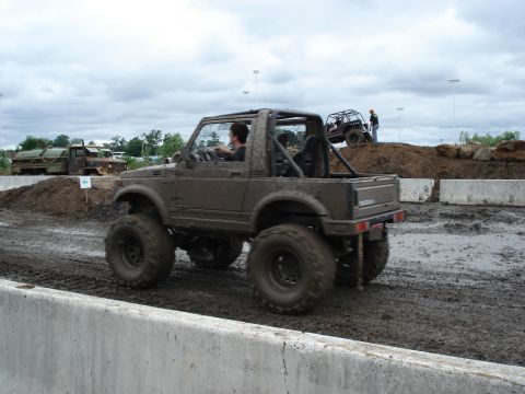 1988 Suzuki Samurai - A heavily modified 1988 Suzuki Samurai navigates a muddy course, with another off-road vehicle visible on a dirt mound.