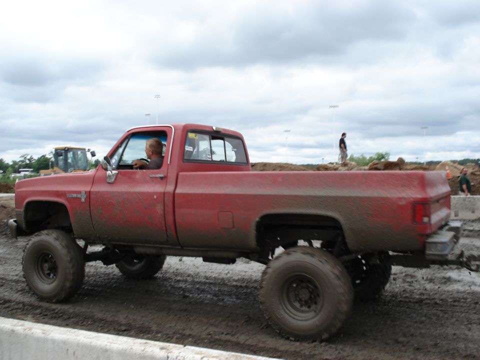 red pickup truck with big tires driving through mud
