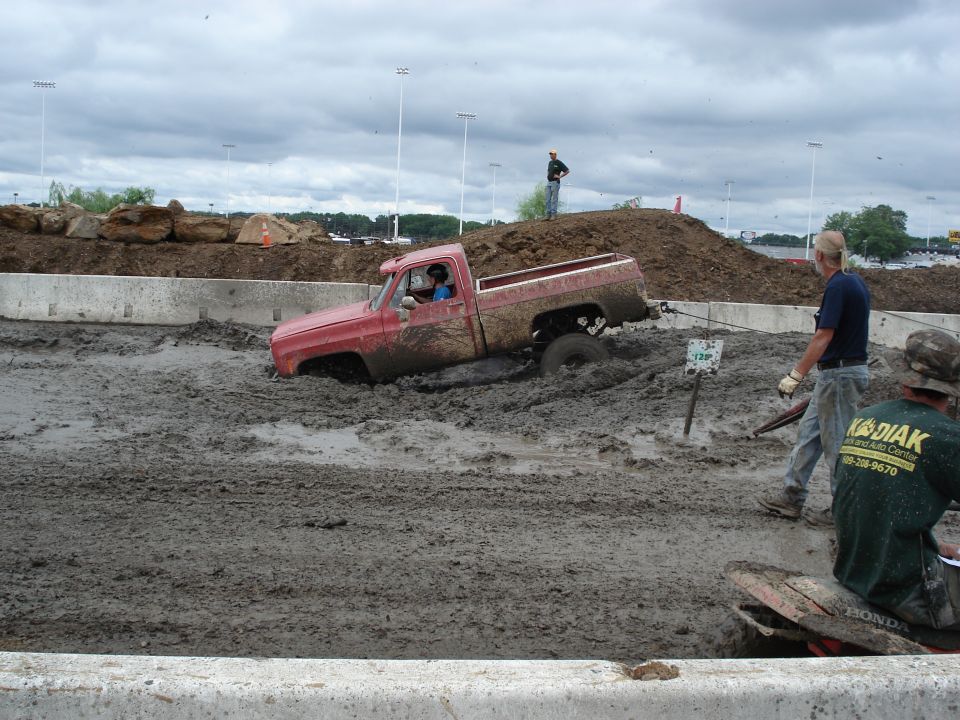 Red pickup truck stuck in mud, driver visible, tow rope attached