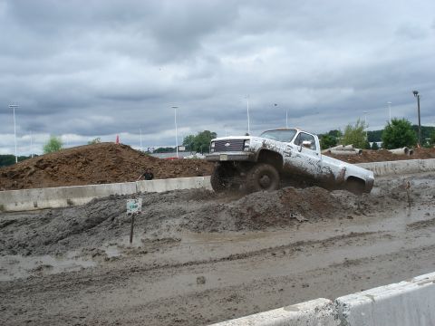 1988 Suzuki Samurai - A white pickup truck powers through a muddy course, kicking up dirt and water.