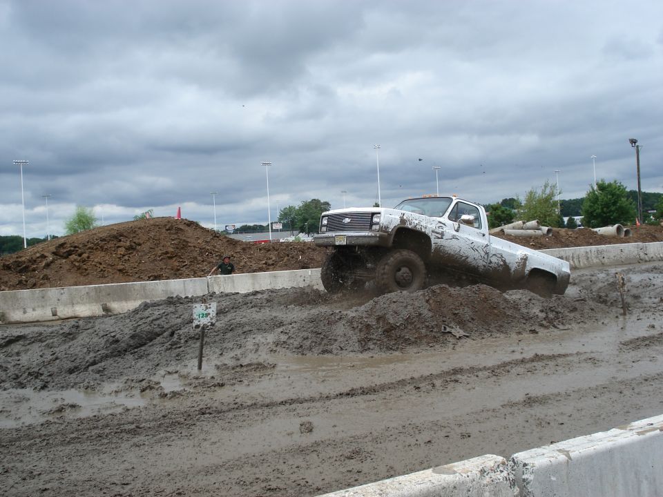 White pickup truck navigating a mud bog, splashing mud