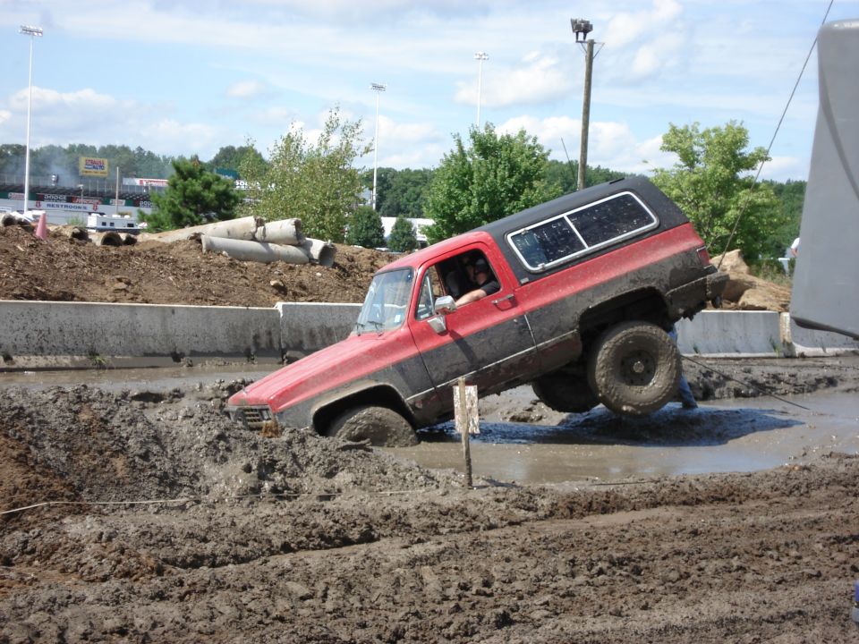 Red and black SUV with lifted suspension stuck in mud, driver visible