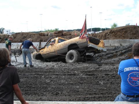 1988 Suzuki Samurai - A yellow pickup truck is stuck deep in mud during a mud bog event, with people attempting to help.