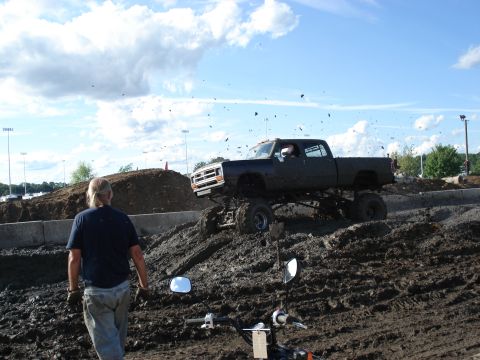 1988 Suzuki Samurai - A lifted pickup truck navigates a muddy track, kicking up dirt under a cloudy sky.