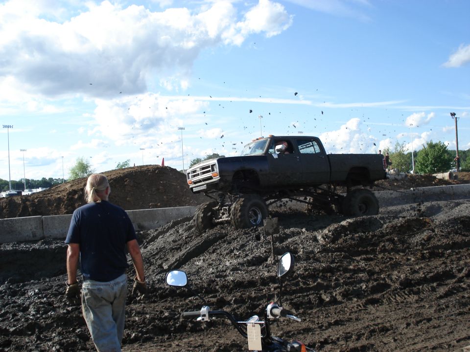 lifted pickup truck driving through mud, person watching
