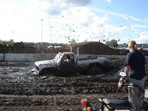 1988 Suzuki Samurai - A white pickup truck is stuck deep in mud during a mud bog event, with a person watching from the side.