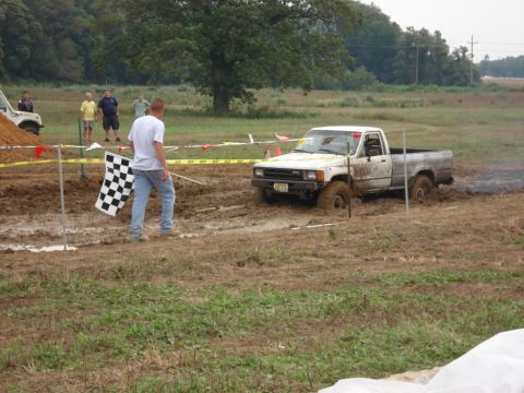 1988 Suzuki Samurai - Mud bog event with a pickup truck stuck in the mire. A checkered flag signals the end of the course.