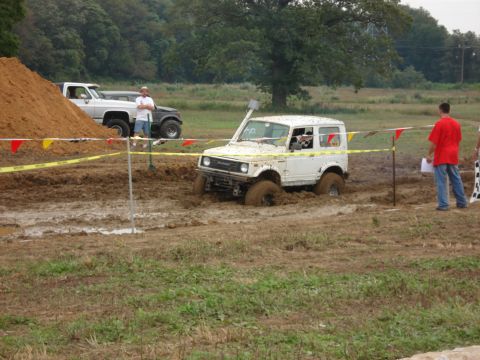 1988 Suzuki Samurai - A white Suzuki Samurai is stuck in a mud pit during an off-road event, with spectators nearby.
