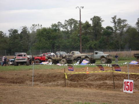 1988 Suzuki Samurai - Modified trucks are parked on the grass near a mud racing course with checkered flags and a numbered sign.