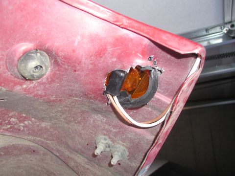 1998 Jeep TJ - Damaged amber marker light assembly on red vehicle body panel, showing exposed wires and broken lens.