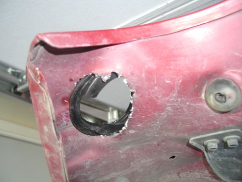 1998 Jeep TJ - A close-up view of a red vehicle body panel shows a freshly cut hole with a rubber grommet installed.