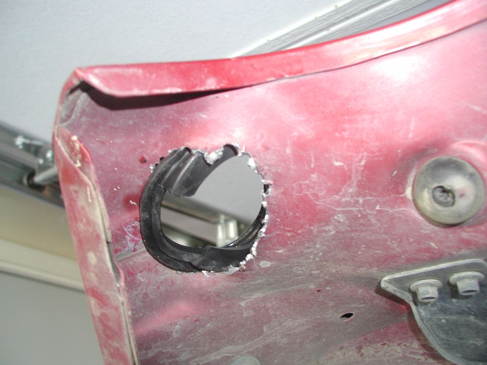 close-up of a red vehicle body panel with a rough hole cut into it, rubber grommet visible inside the hole