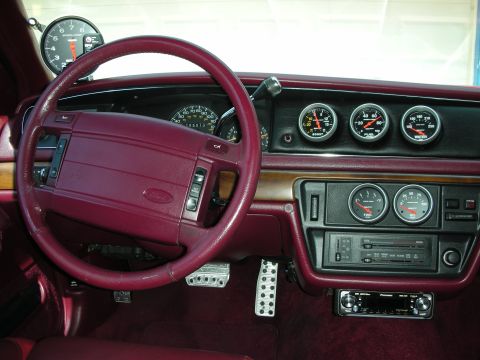 1992 Ford Crown Victoria - Interior dash view of a car with a burgundy/maroon steering wheel, dashboard, and carpet, featuring a Ford horn pad and aftermarket Auto Me…