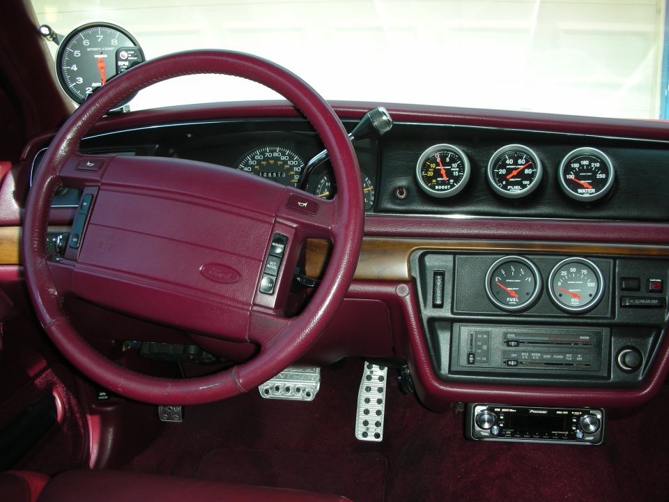 Maroon car interior with steering wheel, aftermarket gauges, and aluminum pedals