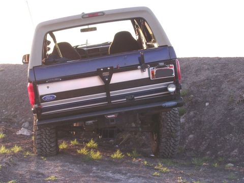 1994 Ford Bronco - This lifted Ford Bronco is shown from the rear, parked on a dirt embankment with the sun low in the sky.