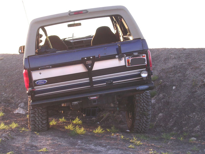 Rear of dark blue Ford Bronco flexing suspension on a dirt hill