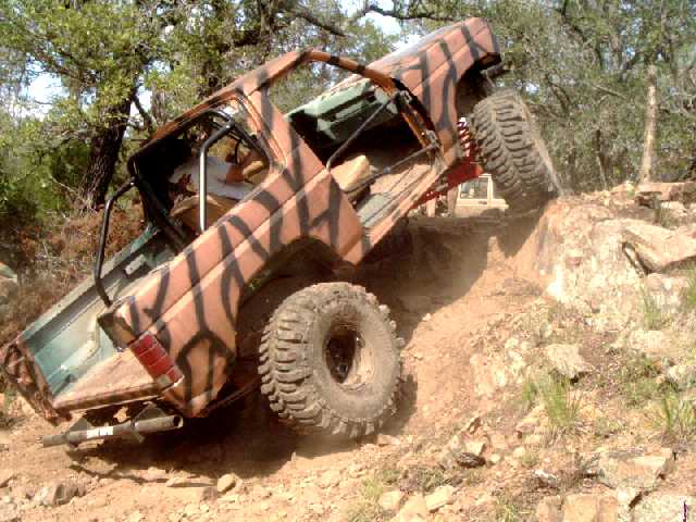 Tiger-striped topless Ford Bronco climbing a steep rock ledge, front wheel up