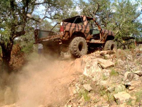 1984 Ford Bronco - This vehicle is navigating a challenging off-road terrain, kicking up a cloud of dust as it ascends the rocky incline.