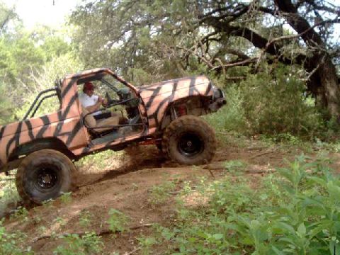 1984 Ford Bronco - Off-road vehicle with tiger stripe paint climbing a dirt hill.
