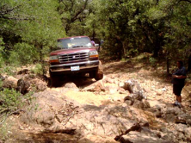 Maroon Ford Bronco 4x4 crawling down a rocky limestone trail with spectators