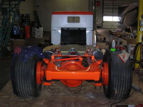 1989 Ford Bronco - The rear axle and suspension of a truck are painted bright orange in a workshop setting.