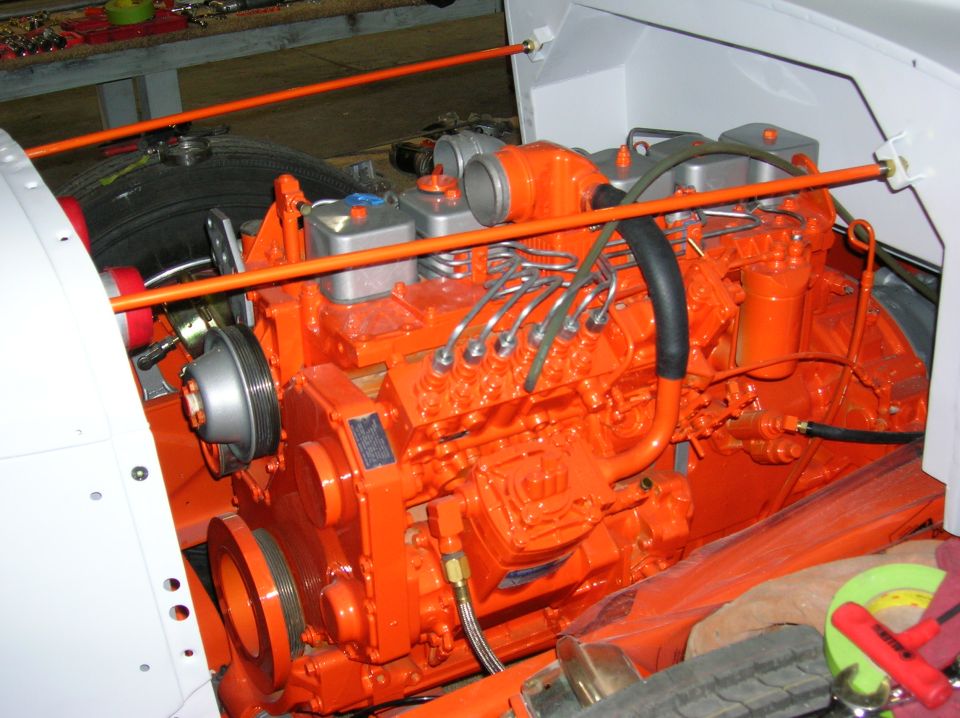 Orange engine with black hoses and silver pulleys, viewed from the side