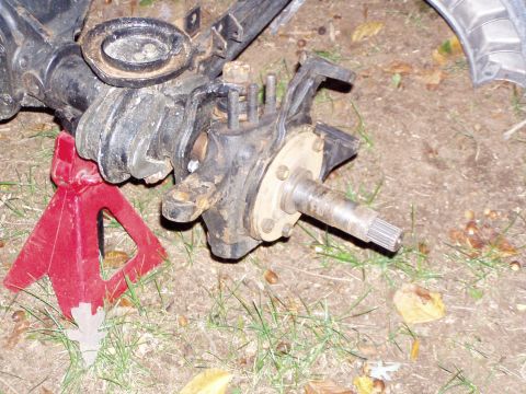 1989 Ford F-250 - A disassembled front axle assembly is supported by a red jack stand on the ground.