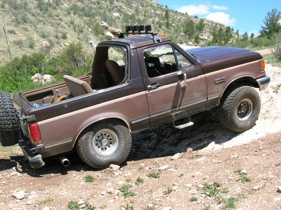 Brown Ford Bronco with off-road tires driving on a rocky trail