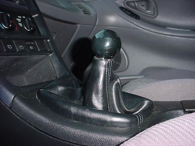 Car interior showing a black leather shift boot and a dark green spherical shift knob. Center console and part of the passenger seat are visible