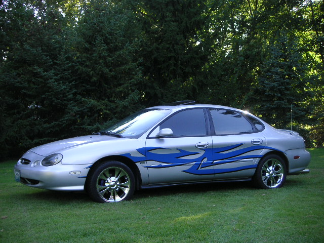 1999 Ford Taurus with blue flame decals on the side, parked on grass