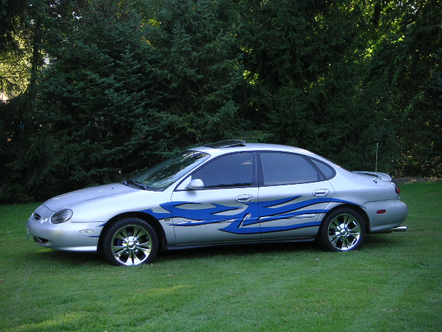 Silver 1999 Ford Taurus sedan with blue flame decals and chrome wheels parked on grass