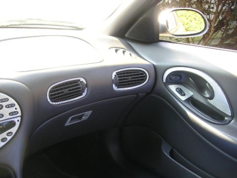 1999 Ford Taurus - The interior of a car is shown, focusing on the dashboard, air vents, and door handle with decorative trim.