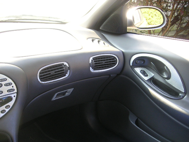 Interior shot of a car's dashboard and door panel, showing air vents and a door handle with carbon fiber trim