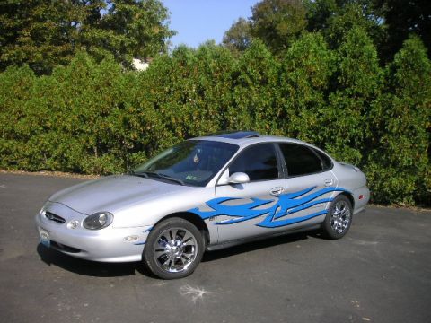 1999 Ford Taurus - This 1999 Ford Taurus features custom blue flame graphics and chrome wheels, parked outdoors.