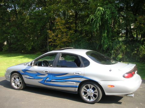 1999 Ford Taurus - Side view of a silver 1999 Ford Taurus custom blue flame graphics and chrome wheels.
