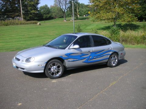 1999 Ford Taurus - A silver sedan with custom blue flame decals is parked outside on a paved surface.