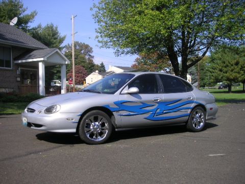 1999 Ford Taurus - This 1999 Ford Taurus features custom blue flame graphics and chrome wheels, parked in a suburban driveway.